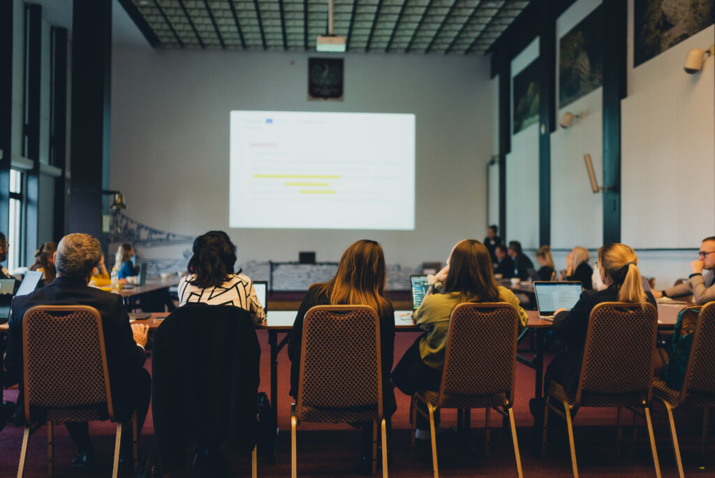Participants attending the AIMused project kick-off meeting, seated at tables and watching a presentation on accessibility and AI in museums.