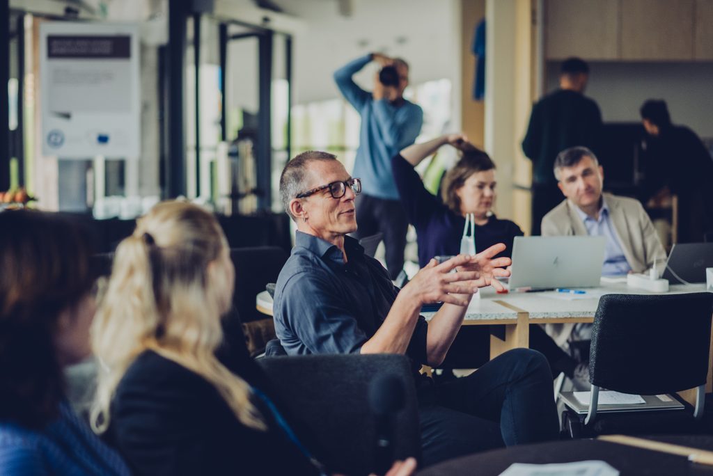 Discussion during the AIMused partner meeting in Klaipėda, with participants seated around tables and exchanging ideas.