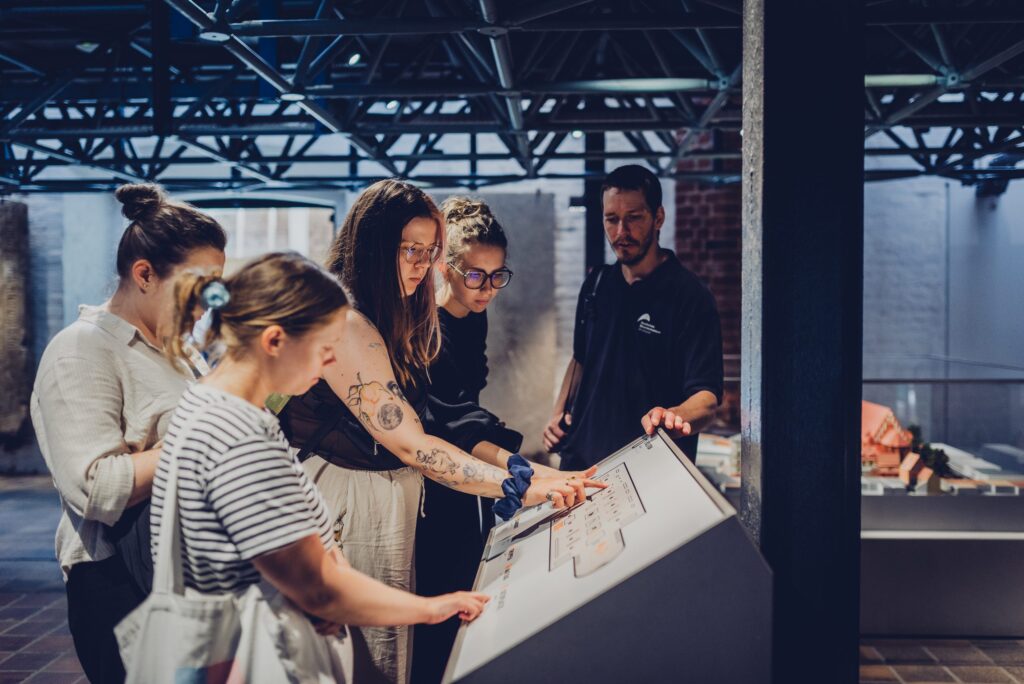 The photo presenting five people examine a tactile museum map, with one person pointing to its raised features.